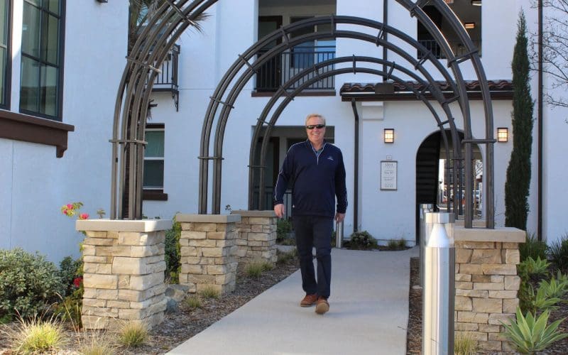 A man walking down the sidewalk of an apartment complex.